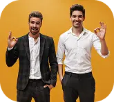 Sarı arka plan önünde poz veren, olumlu el hareketleri yapan, gülümseyen ve kendinden emin görünen iki adam.